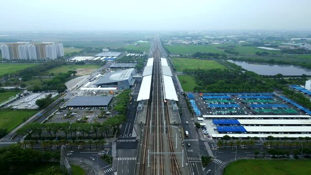 Aerial birds eye shot of Chiayi City Taiwan HSR Train Station with cars on street. Cloudy day with fog in Asia. Agricultural farm fields in rural area.