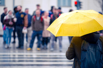 Yellow umbrella against defocused people staying on a crosswalk in the rain