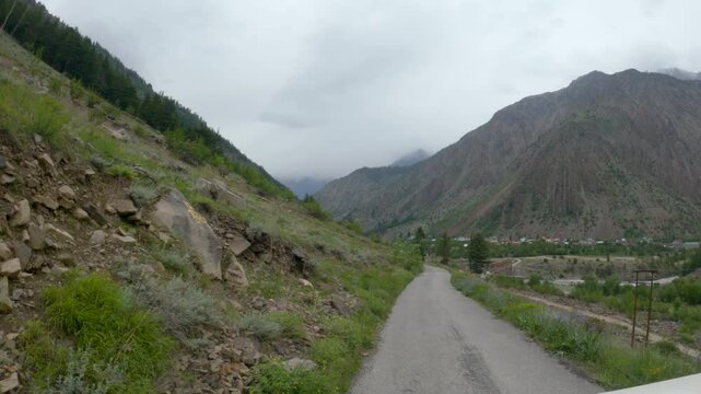 4K POV shot of a vehicle moving on a rural road in front of the Himalayan mountain peaks during a dark cloudy day as seen from Triloknath village in Pattan Valley, Lahaul, Himachal Pradesh, India. 