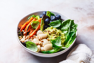 Vegan bowl with butter beans, baked sweet potatoes, guacamole, berries and spinach.