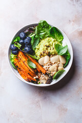 Vegan bowl with butter beans, baked sweet potatoes, guacamole, berries and spinach.