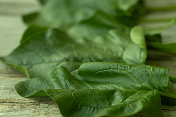 A close-up view of a bright green spinach leaf with visible texture and small water droplets, placed on a rustic wooden surface. Perfect for health and food.