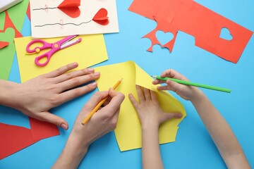 Mother and daughter making handmade project at light blue table, top view