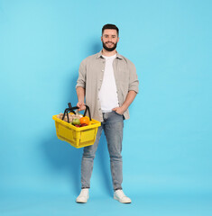 Man with shopping basket full of products on light blue background