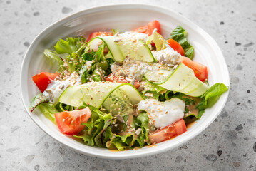 Fresh vegetable salad with lettuce, tomato, cucumber ribbons, sunflower seeds, sesame seeds, and creamy dressing in a white bowl on a speckled countertop.