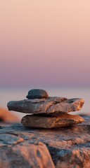 Stacked rocks on a beach with soft pink and blue sky background.