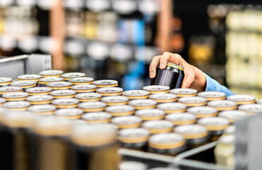 Energy drink or beer can in supermarket. Alcohol aisle in store. Hand taking cola soda beverage in...