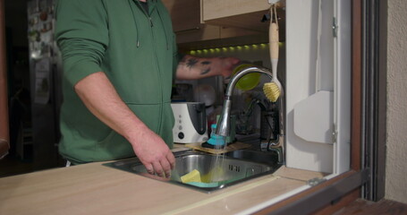 Man washing dishes in a modern kitchen interior, standing by the sink with hands cleaning a bowl, everyday domestic task in a cozy home environment