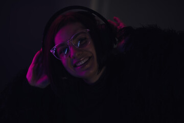 Young woman listening to music using headphones in a dark room with neon light.