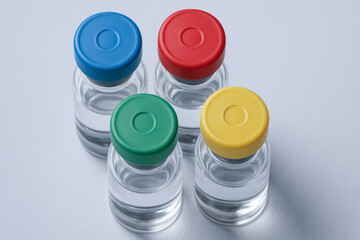 Four clear glass vials with blue, red, green, and yellow caps contain liquid for vaccine production in sterile facility environment
