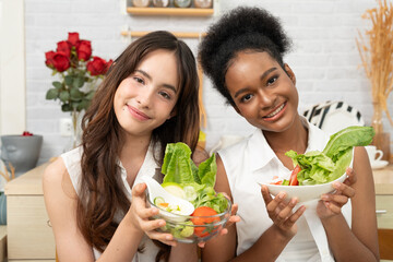Black and white teenage friends working together to make a vegetable salad in the kitchen. Healthy food.