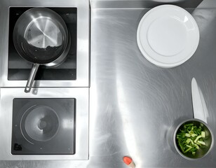 Overhead view of a stainless steel kitchen countertop with induction cooktops, pans, plates, chopped vegetables, and a knife.  Clean, minimalist, modern cooking scene.