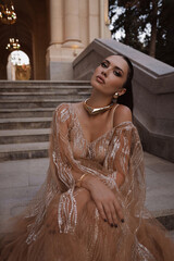 beautiful woman with dark hair in luxurious dress with accessories posing on the stairs of elegant...
