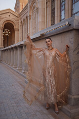 beautiful woman with dark hair in luxurious dress with accessories posing on the stairs of elegant...