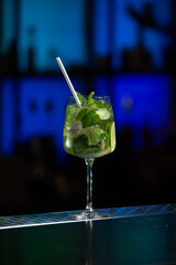 A refreshing green Mojito cocktail, filled with mint leaves, lime slices, and ice, is served in a tall glass with a white straw. © Mykola