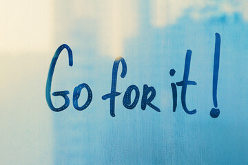 Hand drawn message Go for it on foggy blue glass on city window