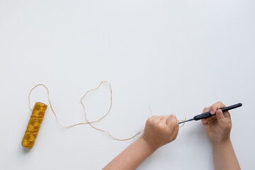 Child crocheting with gold yarn. Hands on creative craft activity for kids