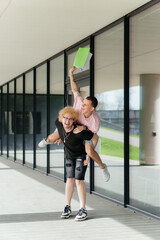 Two cheerful young men celebrate outdoors with a playful piggyback ride and joyful laughter,...