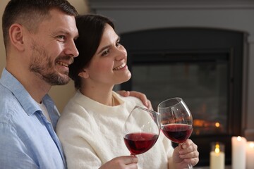 Happy couple clinking glasses of wine near fireplace on floor at home