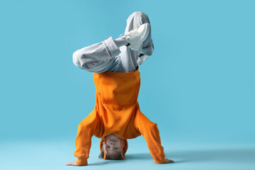 Boy in stylish clothes dancing on light blue background