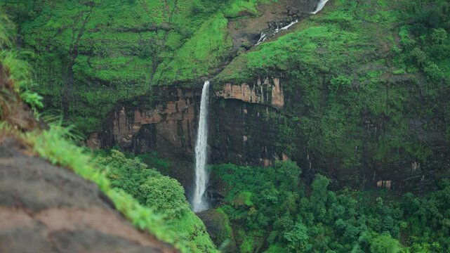 4K Slow motion shot of ring waterfall falling from a mountain cliff as seen from Savlya Ghat view point in Tamhini Ghat near Pune in Maharashtra, India during the monsoon season. Scenic waterfall view