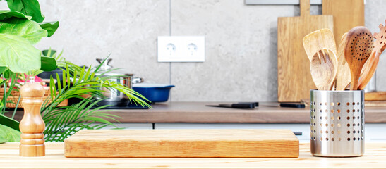 Cozy kitchen wood table with wooden cutting board, spice grinder and utensils, countertop with pans...