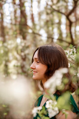 Naklejka premium Smiling young woman in a green dress among white flowers. Joyful and gentle image of spring.