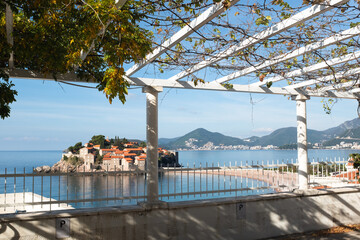 Scenic View of Saint Stefan Island in the Adriatic Sea from a Pergola. The island’s charming architecture and orange rooftops contrast with the deep blue sea. High quality photography