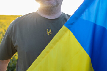 An unrecognizable man in a khaki T-shirt with an embroidered trident and yellow blue flag. Stand...