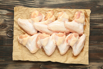 Raw chicken wings on cutting board on brown wooden background.
