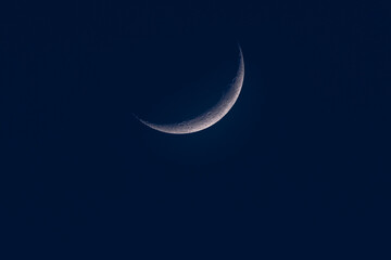 Detailed view of the crescent moon against a deep blue night sky, showing craters and surface texture in stunning clarity.
