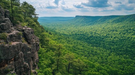 Panoramic view of a lush green valley seen from a rocky clifftop, under a partly cloudy sky