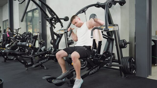 Fitness enthusiast performs chest press motion then removes hand from handle mid rep on weight machine, muscles flexing and equipment steady in modern gym with bright lighting