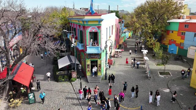 Traditional Caminito passage with tourists and panoramic view of the city from La Boca neighborhood. Aerial camera rises from the street