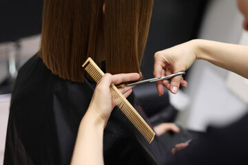 Unrecognisable hairdresser cutting female client hair with professional barber scissors and comb and making stylish haircut short bob hairstyle in beauty salon. Hair care, hair salon and hairstyling