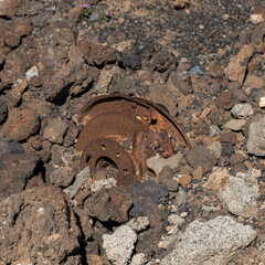 Rusted metal parts, possibly from a car's wheel hub, are surrounded by rugged volcanic rocks in a...