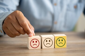 Man hand points on a wooden cube with happy smile face on bright side and unhappy face on dark side of wooden block cube for a positive mindset selection. Emotional state and mental health concept.