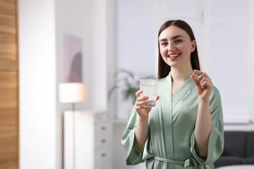 Fotobehang Smiling woman with collagen pill and glass of water at home. Space for text © New Africa