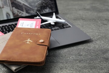 Passports, flight tickets, plane model and laptop on grey table, closeup
