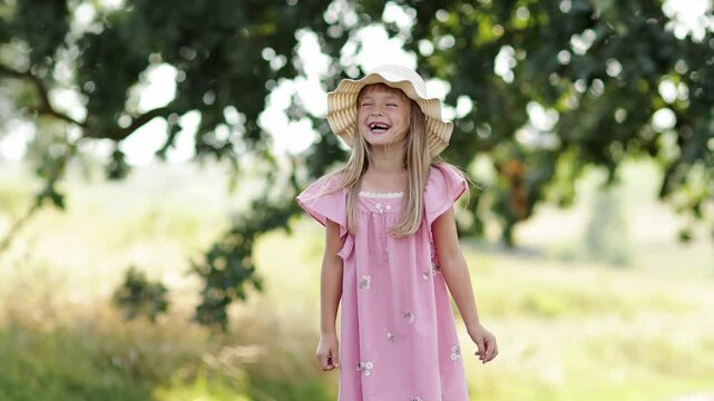 Children's day. Adorable little blonde girl 6-7 years in cute pink dress and straw hat laughing her toothless smile in park on sunny day. Summer holiday vacation outdoors. Happy carefree childhood.