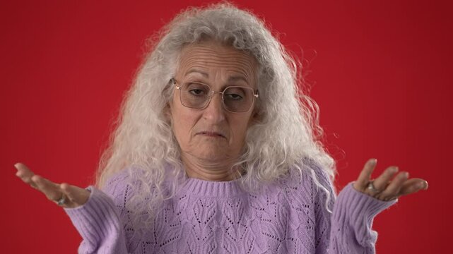 A middle-aged woman with attractive features and glasses gestures I Do Not Know with her hands, conveying a sense of curiosity or uncertainty against a bold red backdrop.