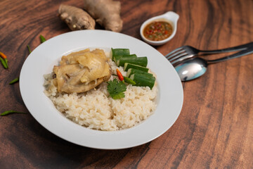 Steamed rice topped with chicken in a white plate on a wooden table