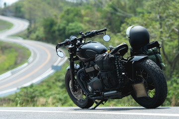 A black motorcycle parked on a scenic, winding road surrounded by lush greenery under daylight.