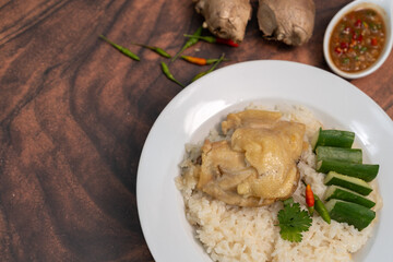 Steamed rice topped with chicken in a white plate on a wooden table