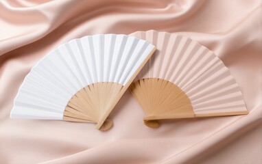 Elegant display of two decorative fans on a soft, pink fabric background, ideal for styling