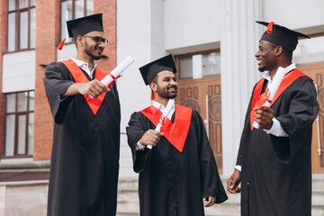 Three happy smiling graduate celebrating graduation in campus with diploma.