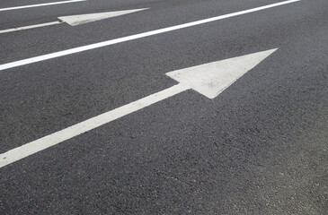 Traffic painted white arrows and lines on asphalt road.