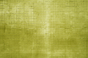 Grungy yellow wall made of small square tiles.