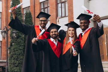 Group of Diverse Happy Graduates Celebrating Achievement Outside University in Cap and Gown