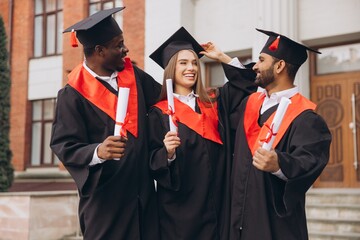 Happy Graduates Celebrating Their Achievement in Traditional Black and Red Gowns Outside University